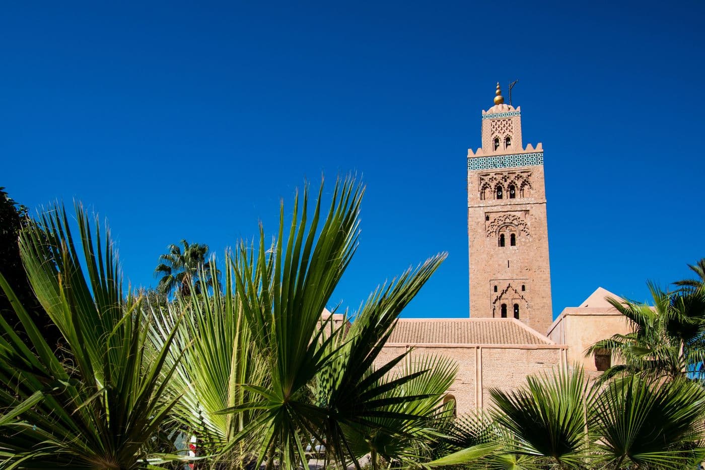 Minaret de la Koutoubia à Marrakech entouré de palmiers sous un ciel bleu